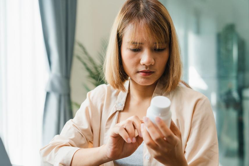 Young person holding medicine bottle searching information online by laptop in living room at home