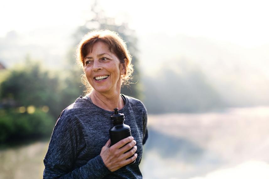 Older person with a water bottle resting after outdoor exercise in nature in the foggy morning