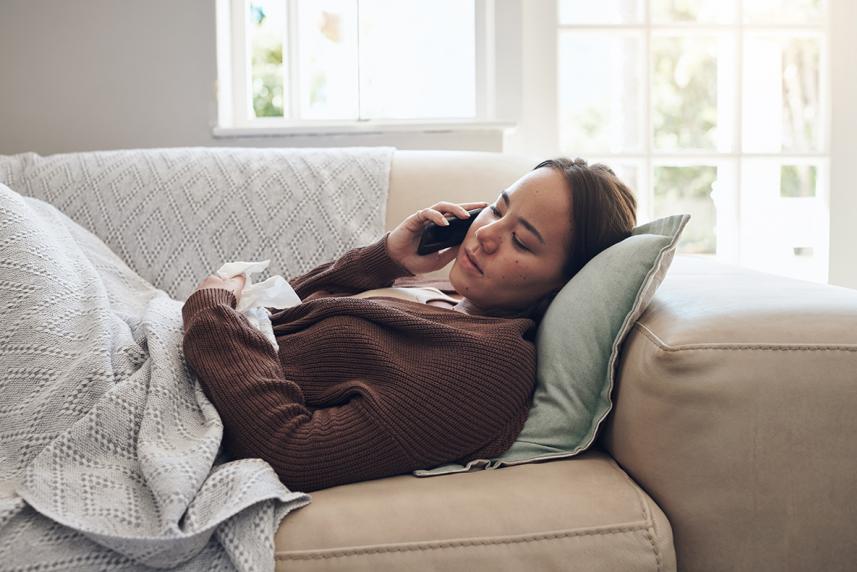 Shot of a young person lying down on the couch talking on a cellphone while feeling sick at home