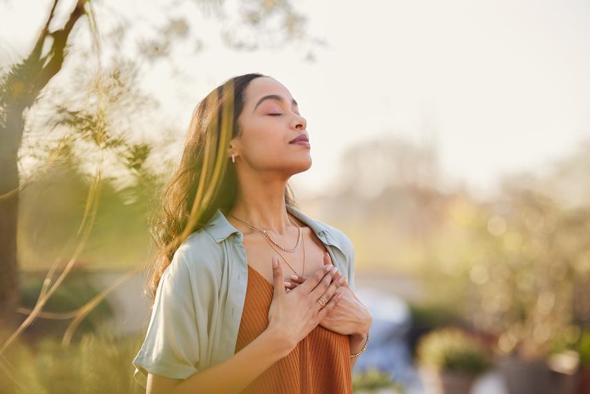 Woman with eyes closed in field with hands on heart