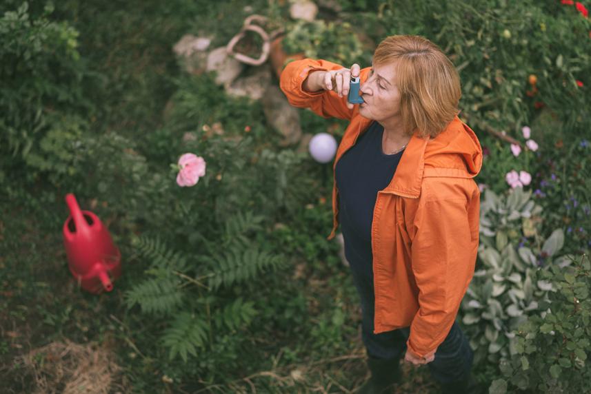 Senior in her 60s using inhaler for asthma or COPD while working in the garden.