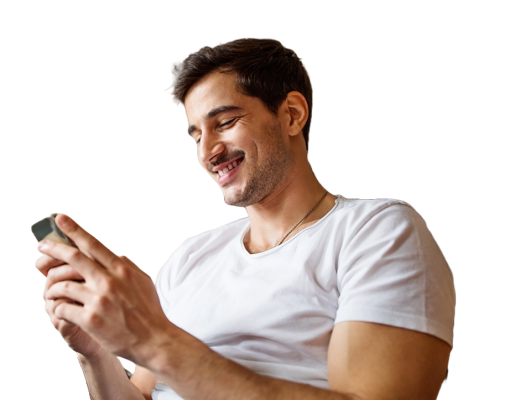 A young man in a t shirt smiling while looking at his phone. 