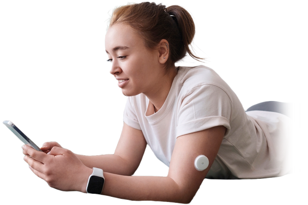 A girl laying on a bed looking at her smart phone. She has a visible medical patch on her arm.
