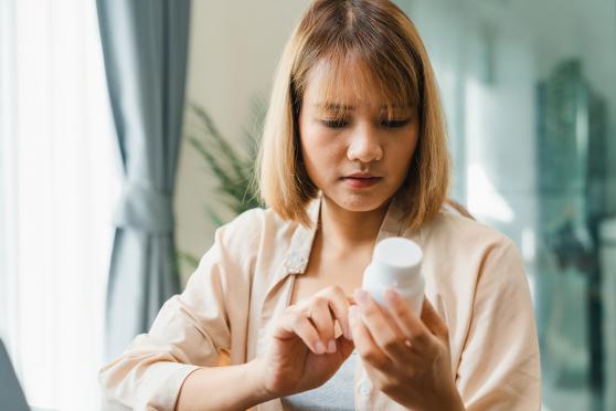 Young person holding medicine bottle searching information online by laptop in living room at home