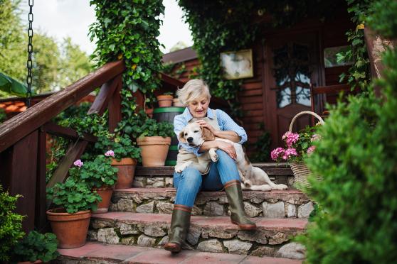 Front view of senior person with a dog sitting on the front steps of a house resting. 