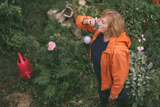 Senior in her 60s using inhaler for asthma or COPD while working in the garden.